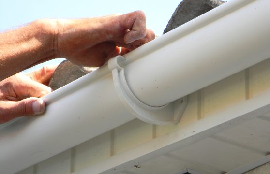 Contractor installing plastic roof gutter. Plastic Roof Guttering Renovation, Rain Guttering Repair & Drainage by Handyman hands.